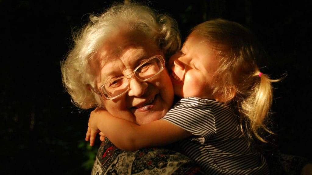 A smiling grandma being hugged and kissed by a grandchild