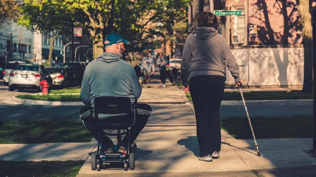 A person in a mobility scooter and a person with a cane walking down the street