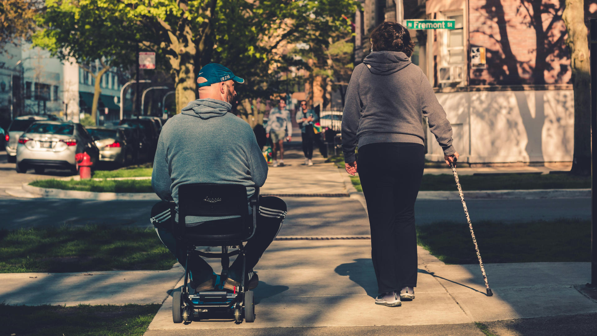 A person in a mobility scooter and a person with a cane walking down the street