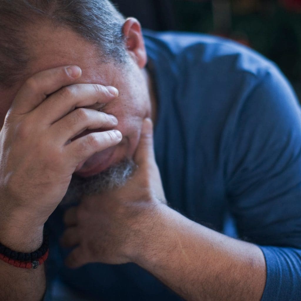 Stressed man hangs his head down with hands on forehead