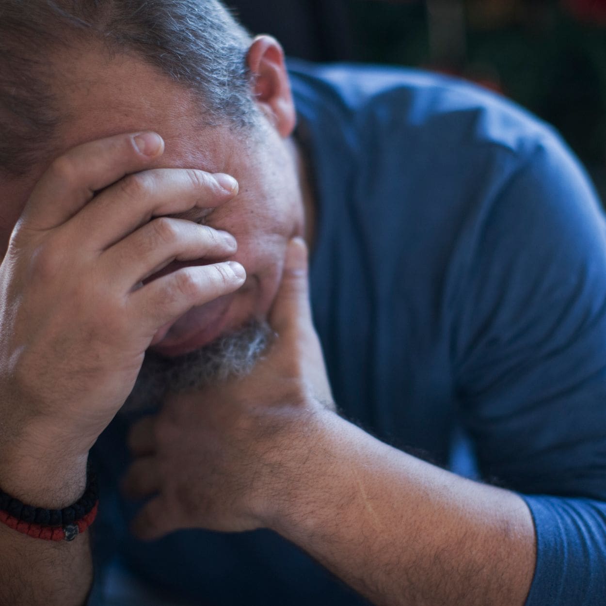 Stressed man hangs his head down with hands on forehead